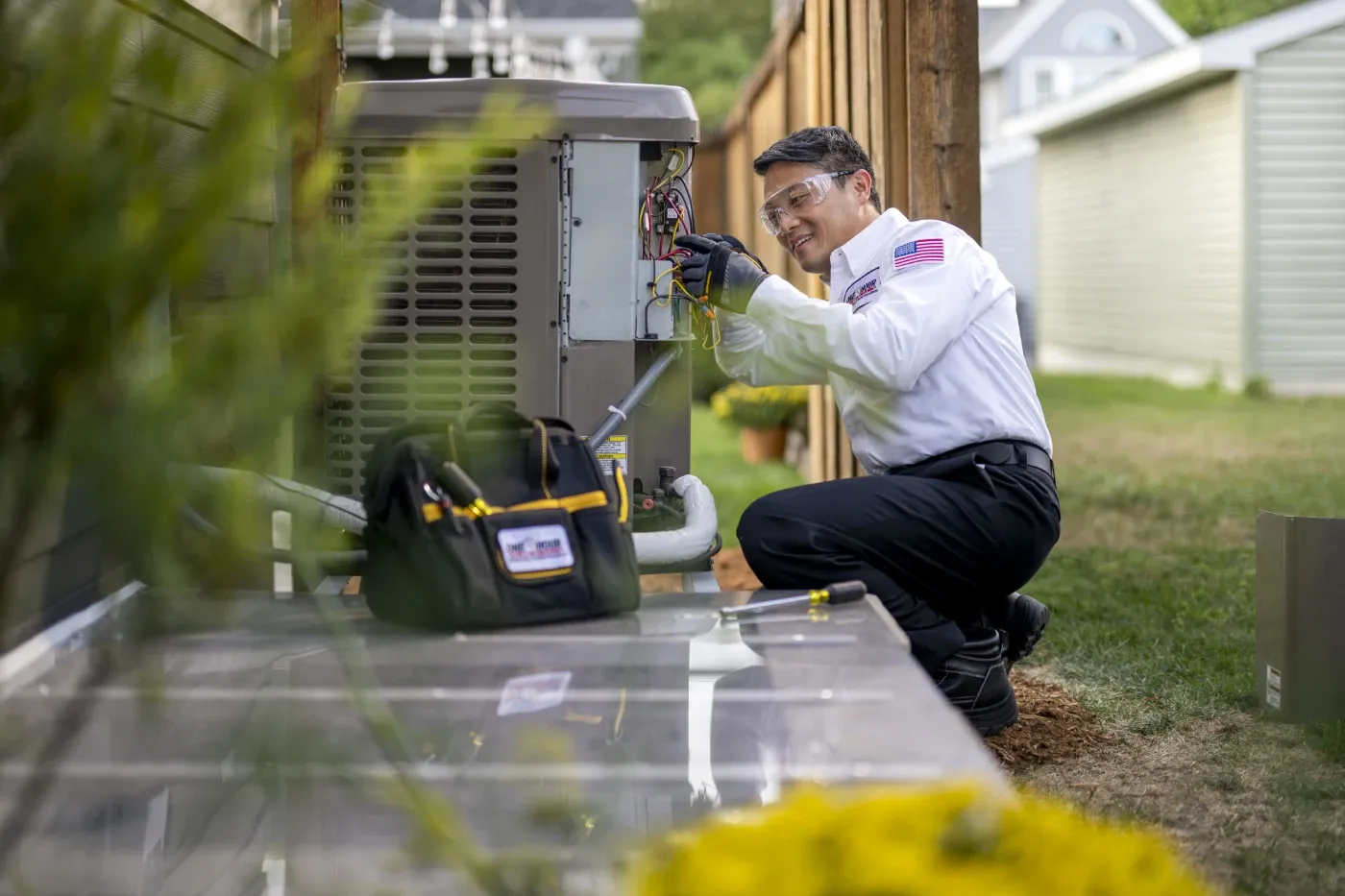Technician servicing residential heating and cooling equipment beside a home